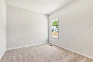 Empty room in Poplar Village, Lot 26, with beige carpet, white walls, and natural light from a single window.