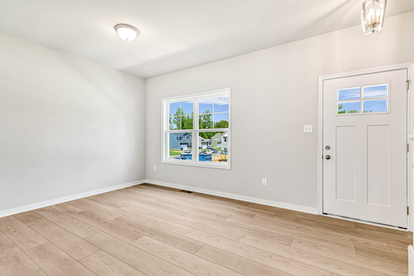 Bright, empty room in Poplar Village with light wood floors, white walls, window, and white front door.