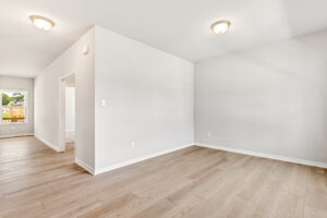 Bright empty room in Poplar Village with light wood flooring, white walls, ceiling lights, and a window. Lot 26.