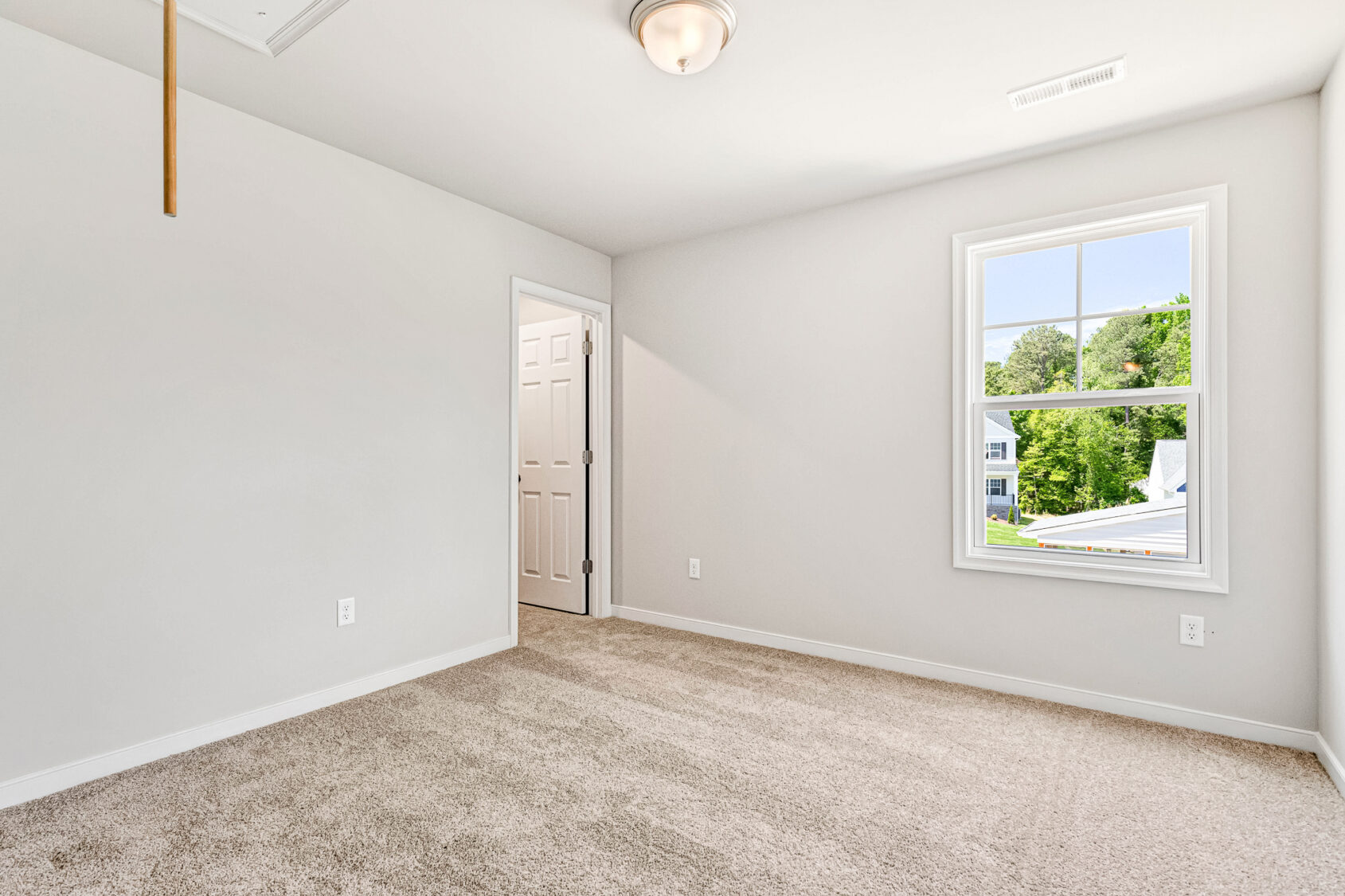 Bright, empty Poplar Village bedroom with beige carpet, white walls, window, and door to another room. Lot 26.