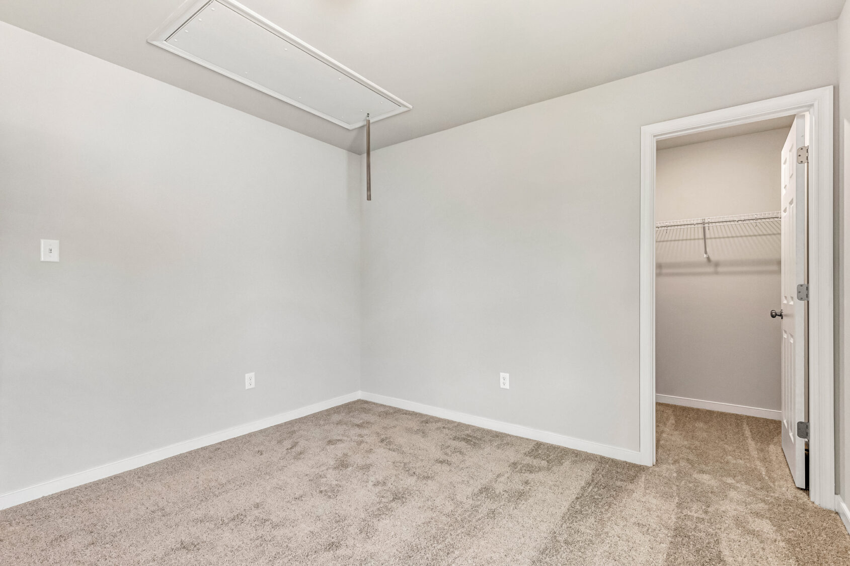 Empty beige carpeted room in Poplar Village with light gray walls, attic door, and open walk-in closet. Lot 26.