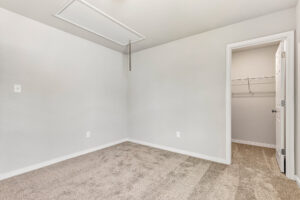 Empty beige carpeted room in Poplar Village with light gray walls, attic door, and open walk-in closet. Lot 26.