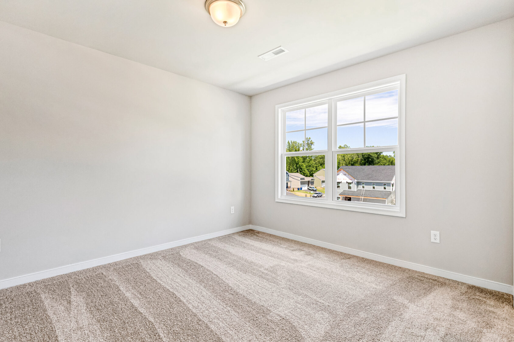 Empty, carpeted room with light walls, ceiling light, and a window overlooking Poplar Village, Lot 26.