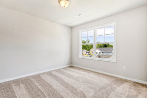 Empty, carpeted room with light walls, ceiling light, and a window overlooking Poplar Village, Lot 26.