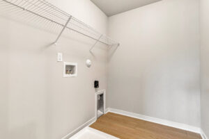 Empty laundry room in Poplar Village Lot 26 with wire shelf, washer/dryer hookups, and light wood flooring.