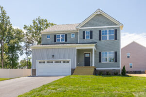 Two-story gray house in Poplar Village with white garage, front porch steps, and lawn on Lot 26.