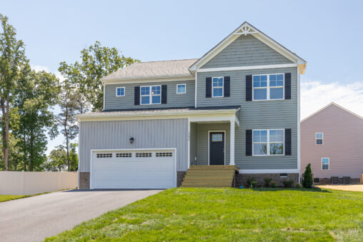 Two-story gray house in Poplar Village with white garage, front porch steps, and lawn on Lot 26.