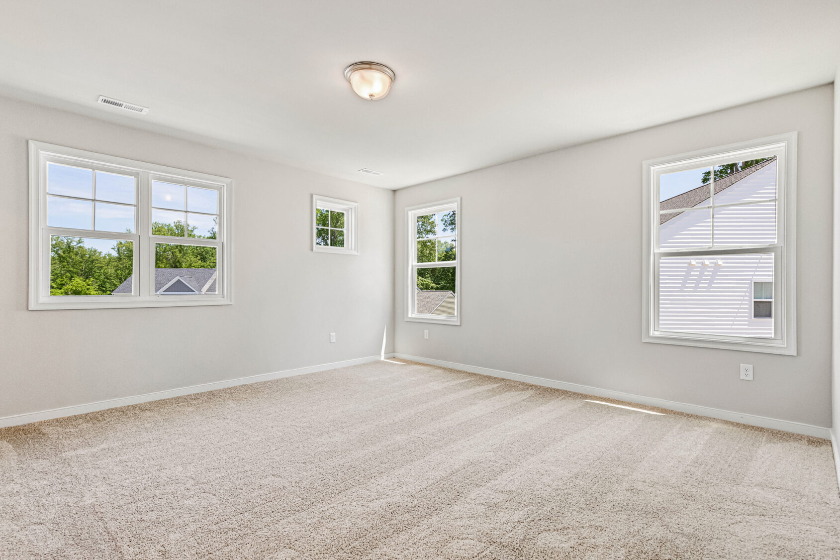 Bright, empty carpeted room in Poplar Village, Lot 26, with three windows, white walls, and a ceiling light fixture.