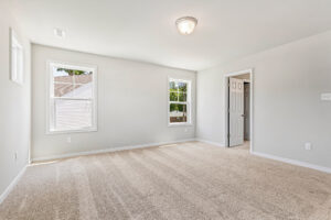Bright, empty carpeted room in Poplar Village with white walls, two windows, ceiling light, and open door.