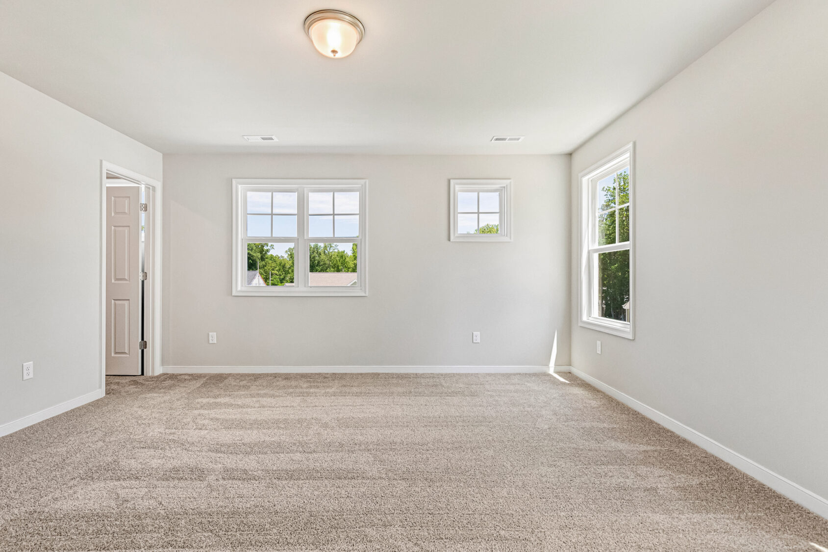 Empty room in Poplar Village, Lot 26 with beige carpet, white walls, three windows, and abundant natural light.