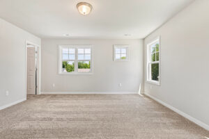 Empty room in Poplar Village, Lot 26 with beige carpet, white walls, three windows, and abundant natural light.