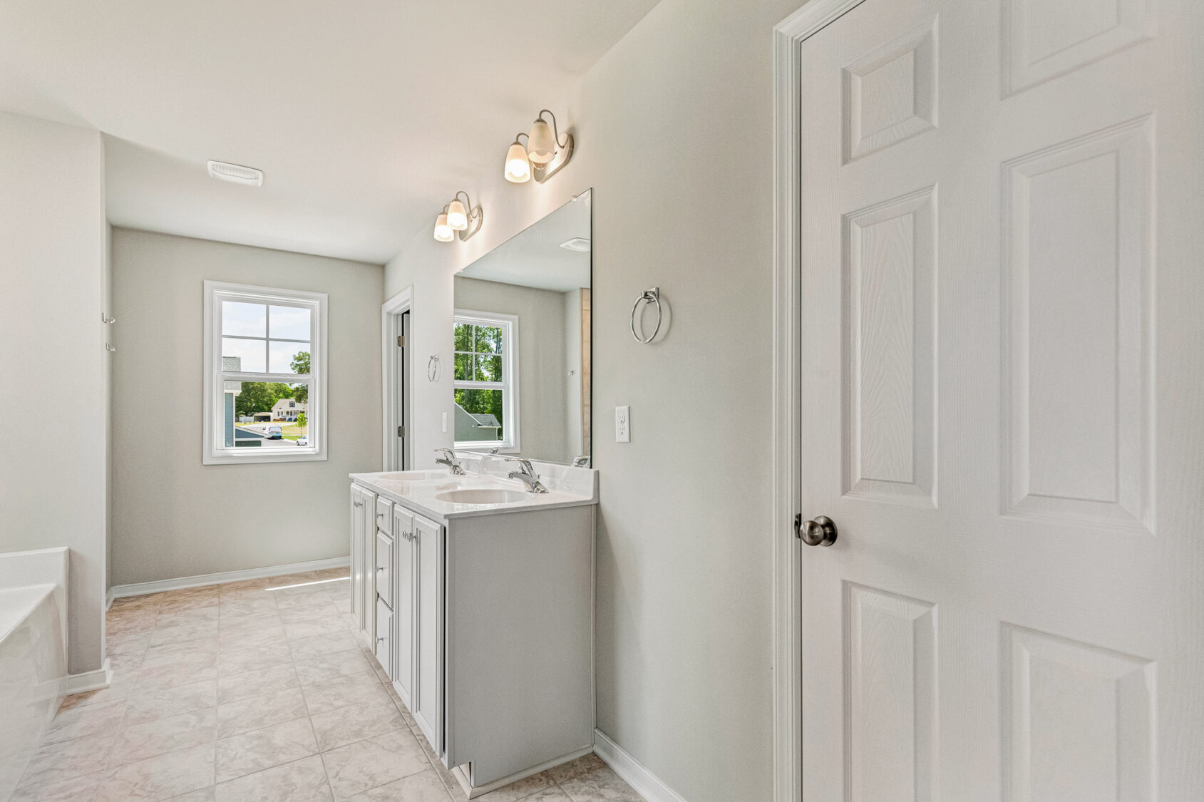 Bright bathroom in Lot 26, Poplar Village with double sink vanity, large mirror, tiled floor, window, and white door.