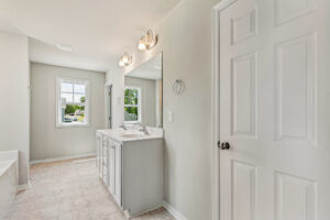 Bright bathroom in Lot 26, Poplar Village with double sink vanity, large mirror, tiled floor, window, and white door.
