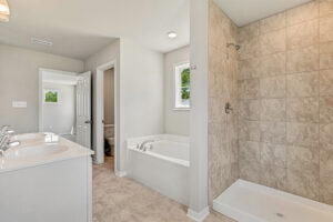 Modern bathroom in Lot 26, Poplar Village, with double sink, separate tub, and tiled walk-in shower with a window.