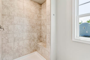Walk-in shower with beige tiles, a built-in bench, and natural light in Lot 26 of Poplar Village.