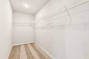 Empty Poplar Village walk-in closet with beige carpet, white walls, and wire shelves on both sides under ceiling light.