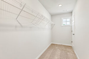 Empty walk-in closet with beige carpet, white walls, wire shelving, and a window in Poplar Village Lot 26.