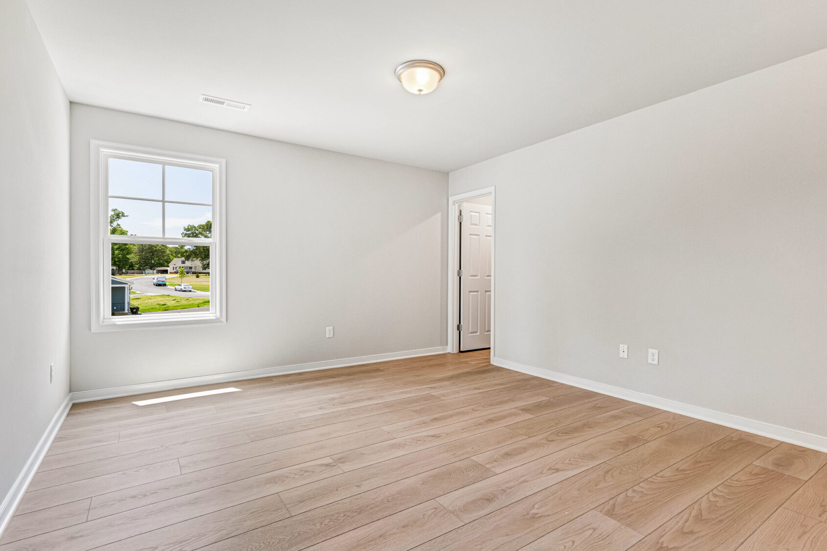 Bright, empty room in Poplar Village with light wood floors, white walls, window, and door leading to another space.