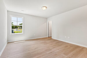 Bright, empty room in Poplar Village with light wood floors, white walls, window, and door leading to another space.