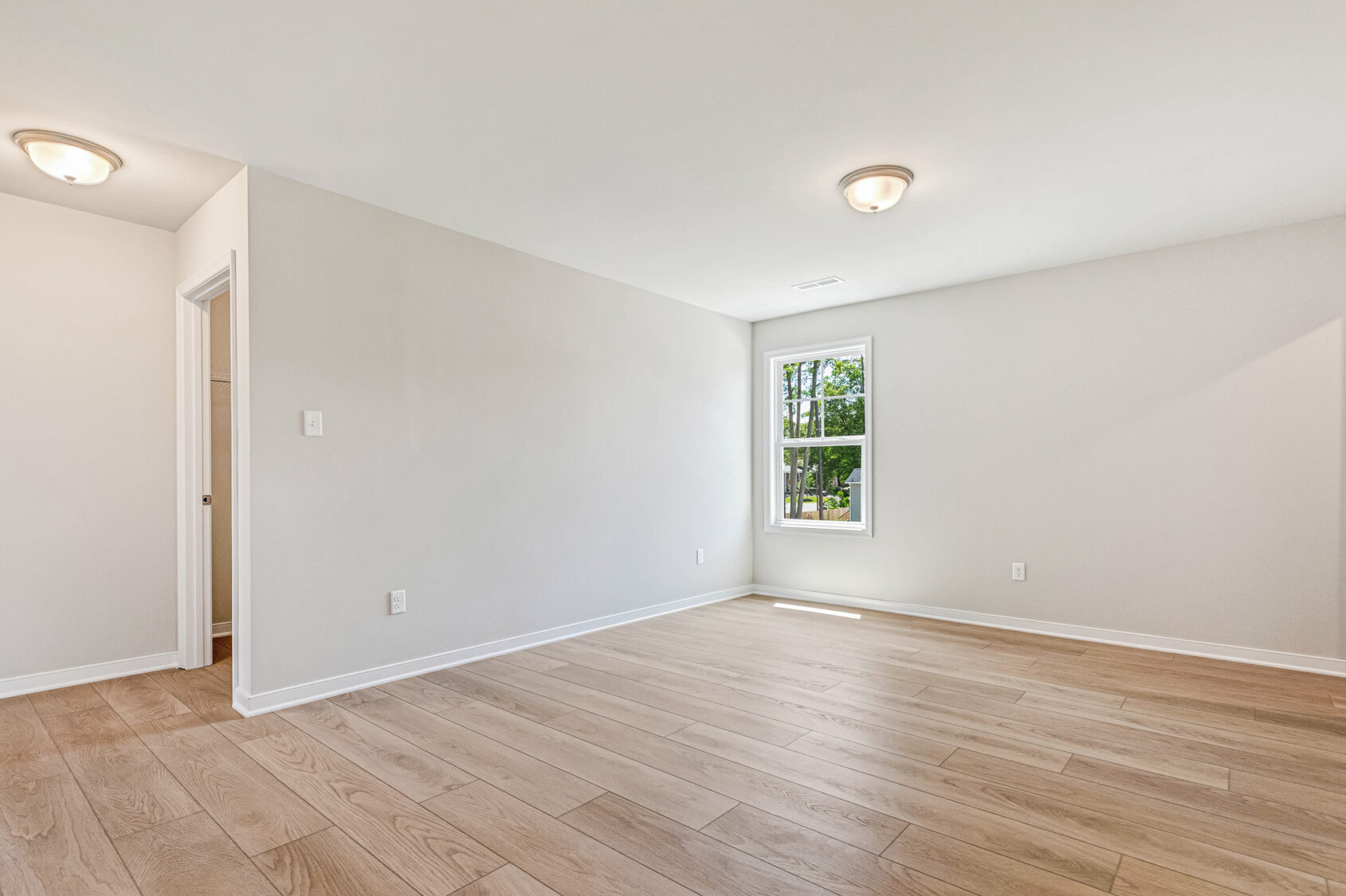 Bright, empty room in Poplar Village with light wood floors, white walls, and a window letting in natural light.