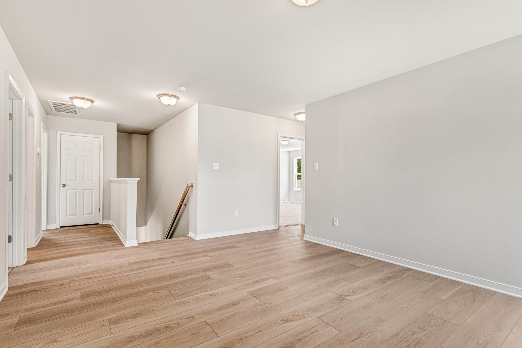 Bright empty room with light wood flooring in Poplar Village, Lot 26; white walls and multiple doorways to other rooms.