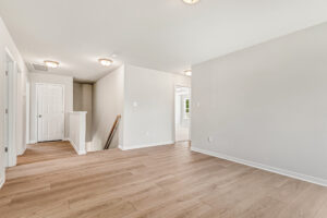 Bright empty room with light wood flooring in Poplar Village, Lot 26; white walls and multiple doorways to other rooms.