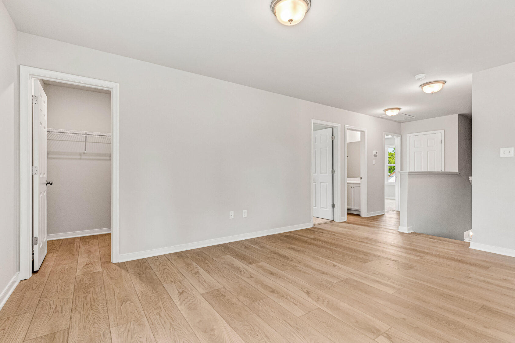 Bright, empty room in Poplar Village with light wood flooring, white walls, and open doors to closets and hallway.
