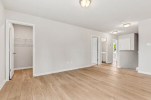 Bright, empty room in Poplar Village with light wood flooring, white walls, and open doors to closets and hallway.