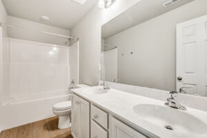 Bright Poplar Village bathroom with double sinks, white cabinets, a large mirror, and a bathtub with shower curtain rod.