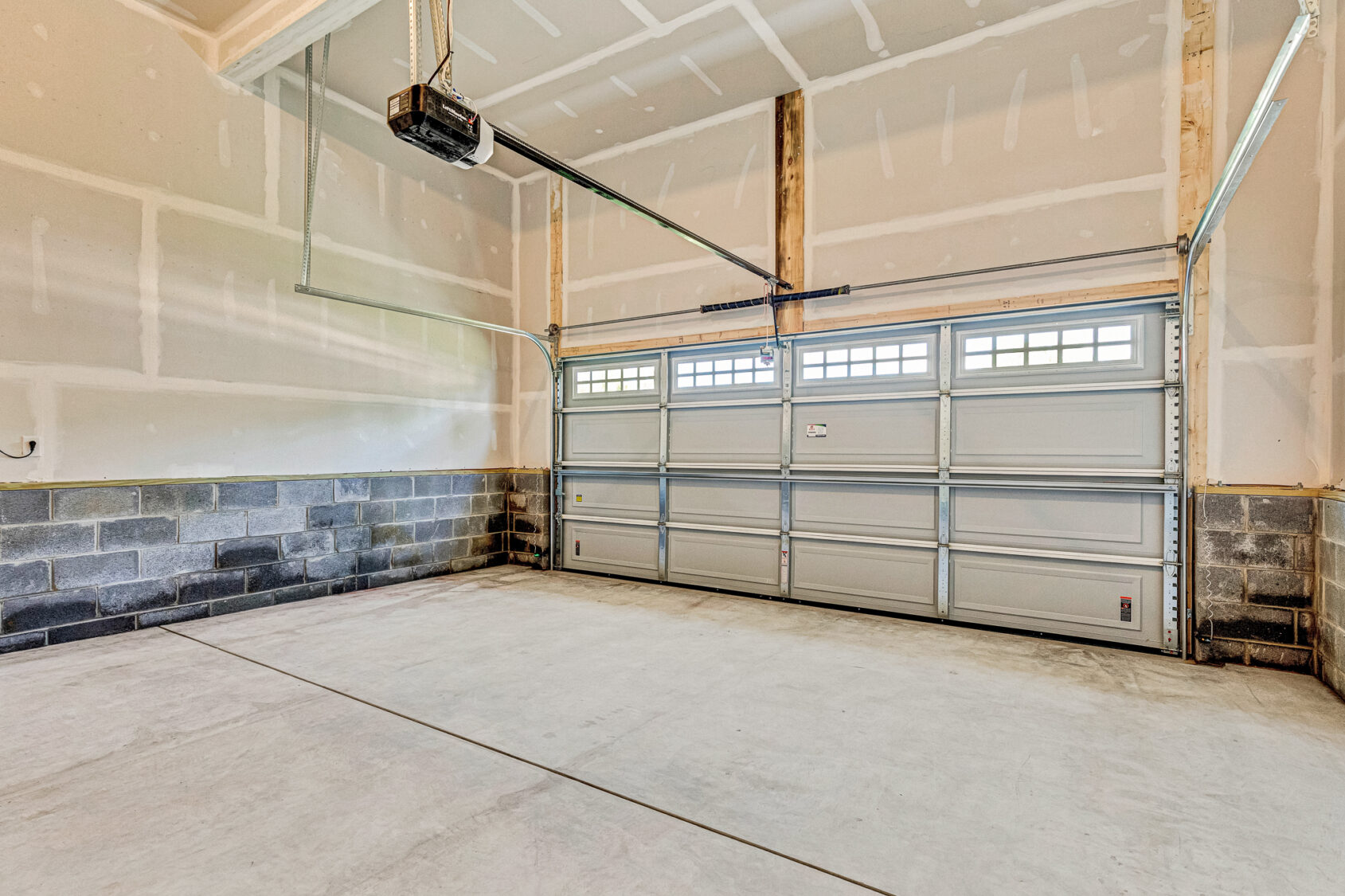 Empty, unfinished garage on Lot 26 in Poplar Village with closed double doors and exposed drywall and concrete block walls.
