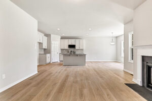 Open kitchen and living area in Poplar Village Lot 26 with light wood floors, white cabinets, and natural light.