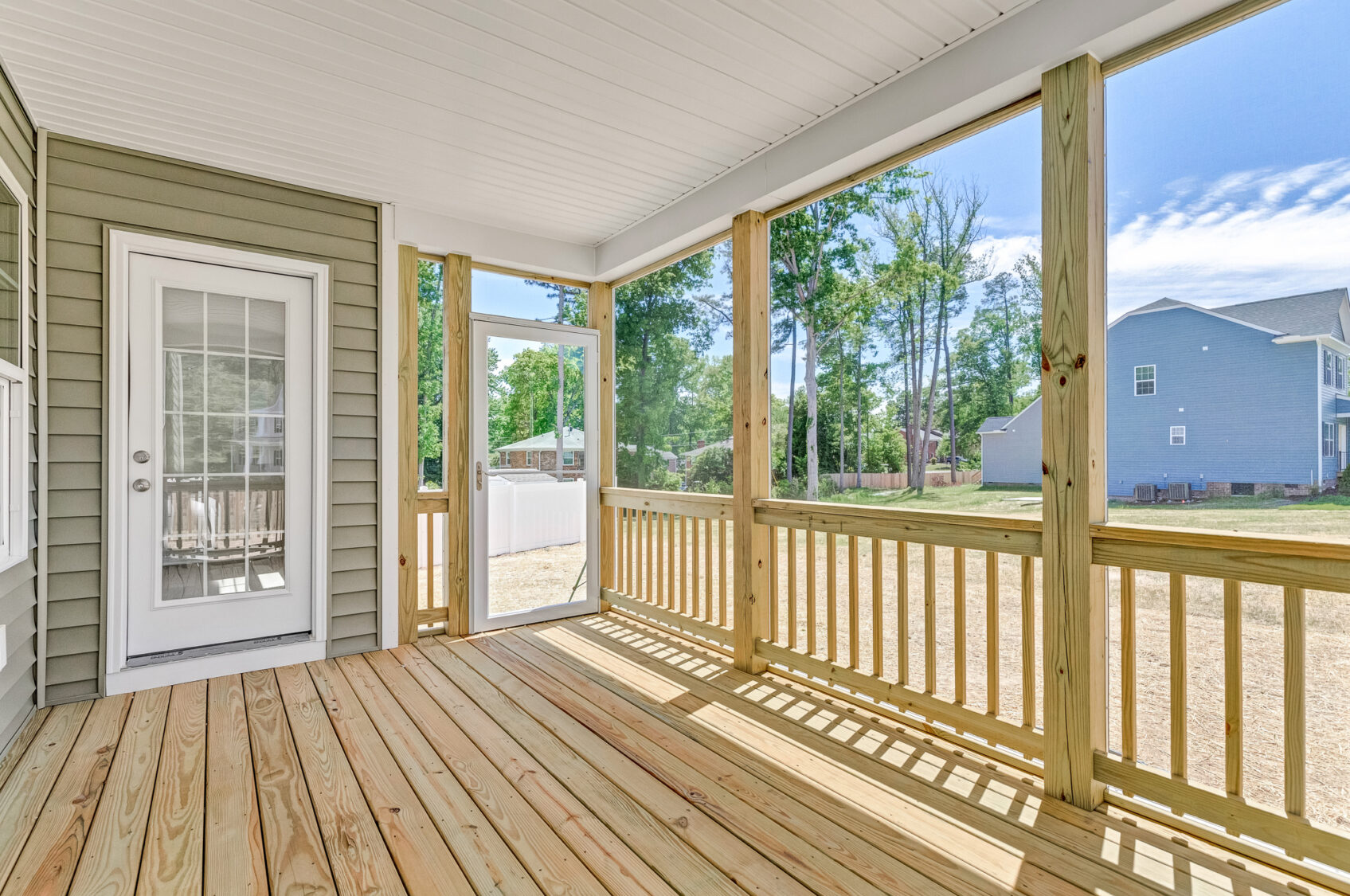A screened-in porch with wooden flooring overlooks the sunny yard of Lot 26 in Poplar Village.
