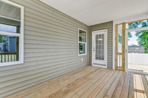 Enclosed porch at Lot 26 in Poplar Village with light wood flooring, gray siding, two windows, and a glass door outside.