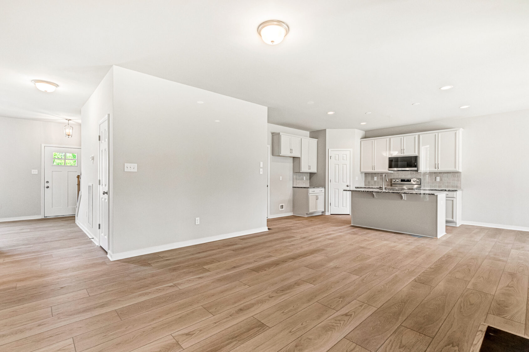 Open concept kitchen and living area in Poplar Village Lot 26, featuring wood floors and modern light fixtures.