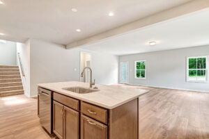 Modern open kitchen with island sink and wood cabinets at Somerset Hill, Lot 8, plus bright living room views and stairs.