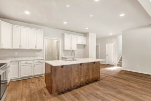 Bright kitchen in Lot 8, Somerset Hill: white cabinets, wood island, marble countertops, and stairs in the background.