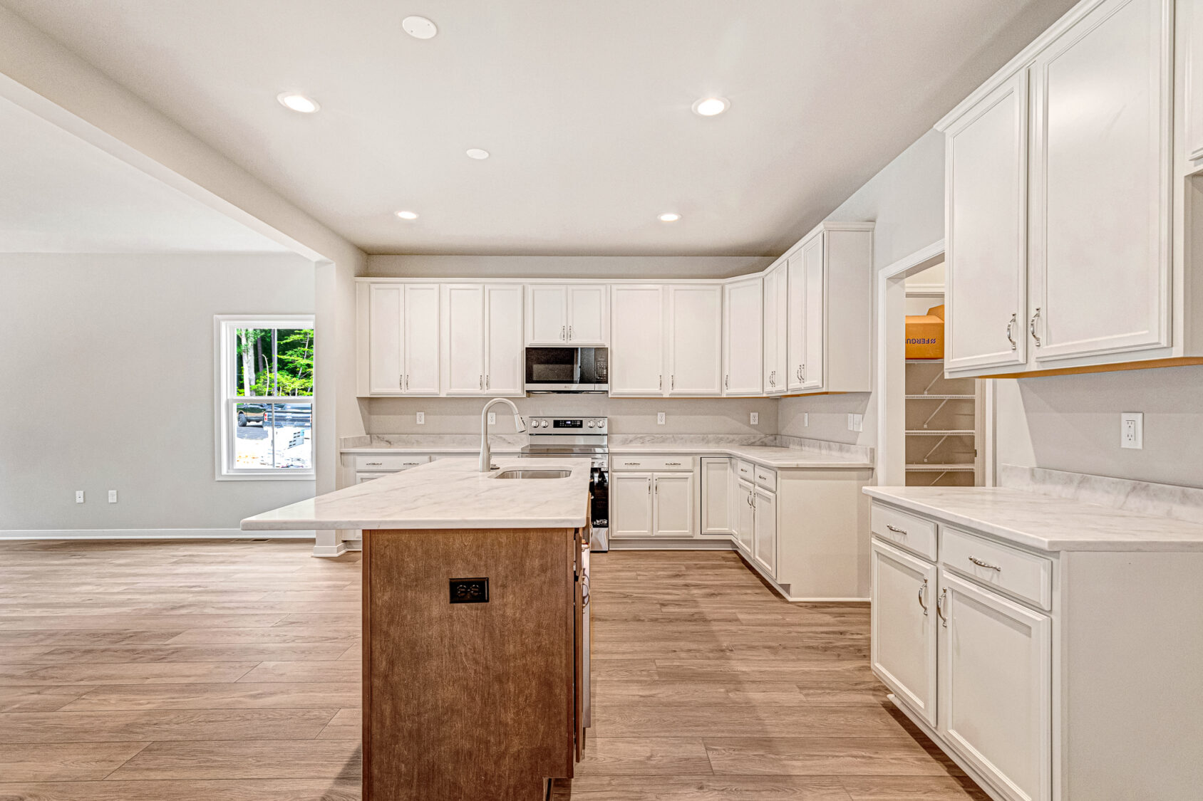 Modern kitchen in Lot 8, Somerset Hill, with white cabinets, stainless appliances, island, wood floor, and walk-in pantry.