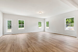 Spacious empty room at Somerset Hill's Lot 8, with wood floors, white walls, and large windows for natural light.