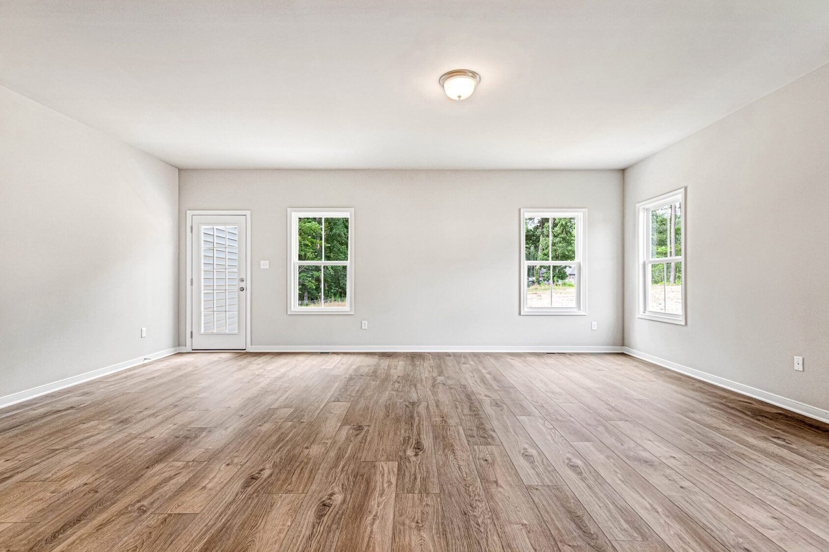 Empty room at Somerset Hill, Lot 8, features wood flooring, white walls, three windows, and a glass-paneled door.