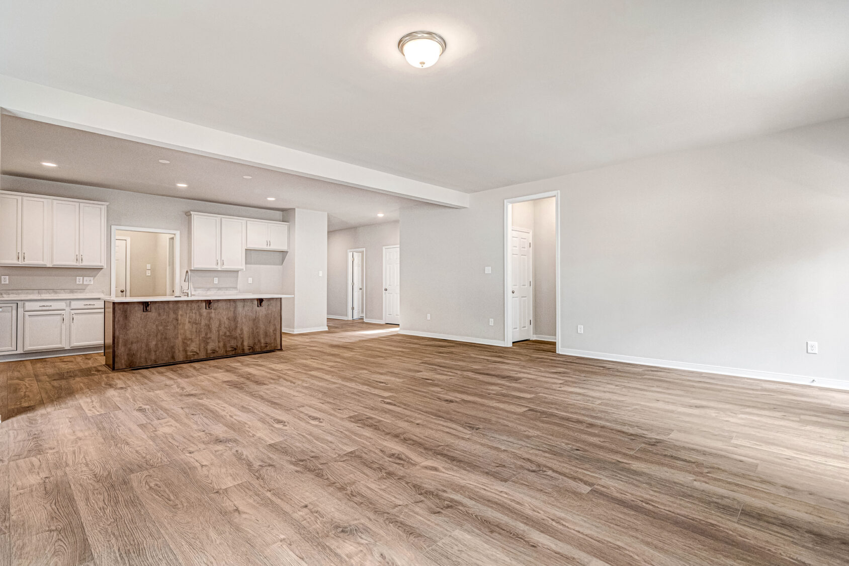 Spacious empty room with wood floors, white walls, ceiling light, and an open kitchen in Somerset Hill Lot 8.
