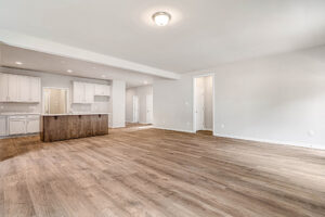 Spacious empty room with wood floors, white walls, ceiling light, and an open kitchen in Somerset Hill Lot 8.