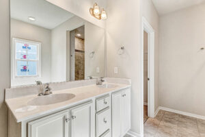 Bright Somerset Hill bathroom with double sinks, large mirror, white cabinets, light fixture, and tile floor.