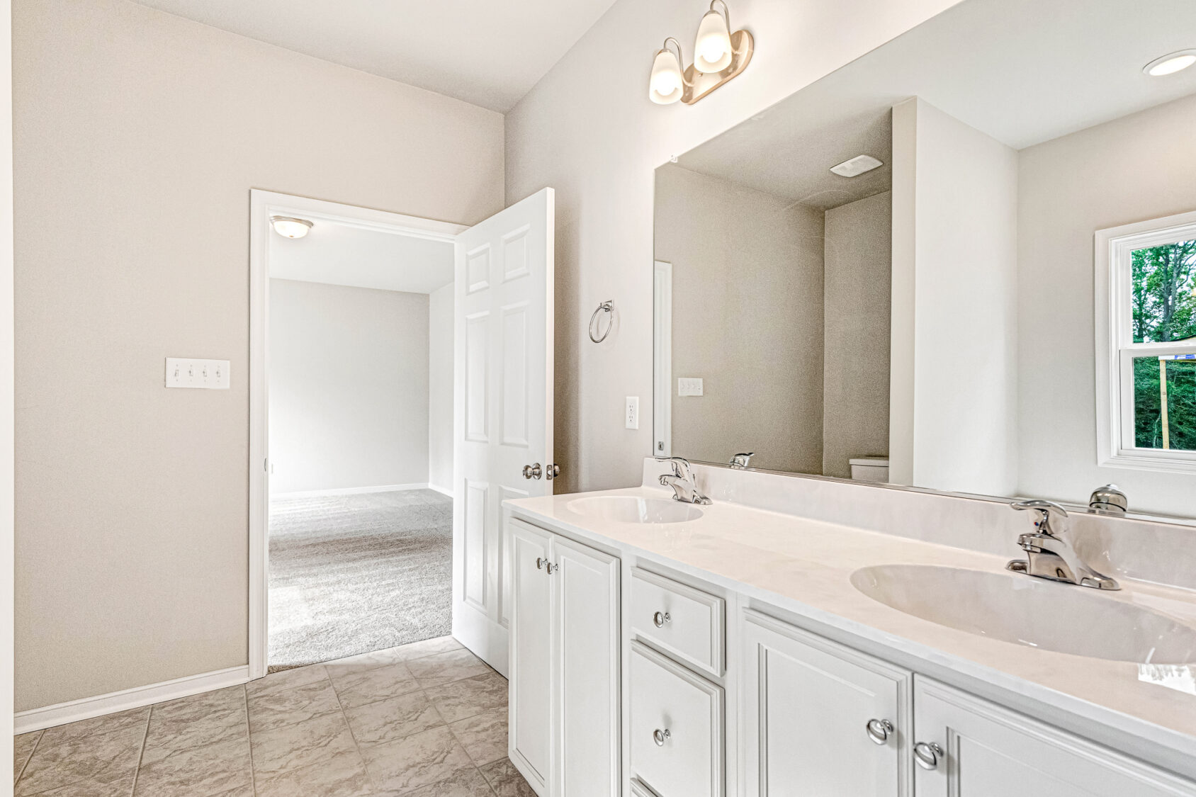 Bright Somerset Hill bathroom with double sinks, white cabinets, and a view into Lot 8's adjacent carpeted room.