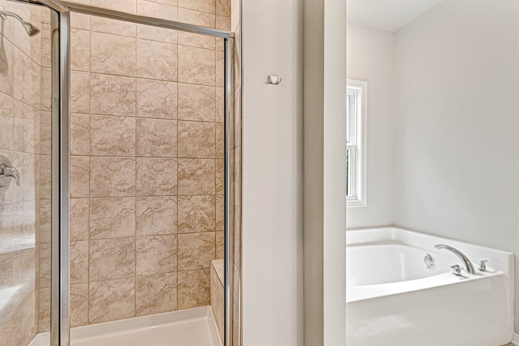 Glass shower with beige tiles, Lot 8 Somerset Hill, next to a white bathtub under a window in a bright bathroom.