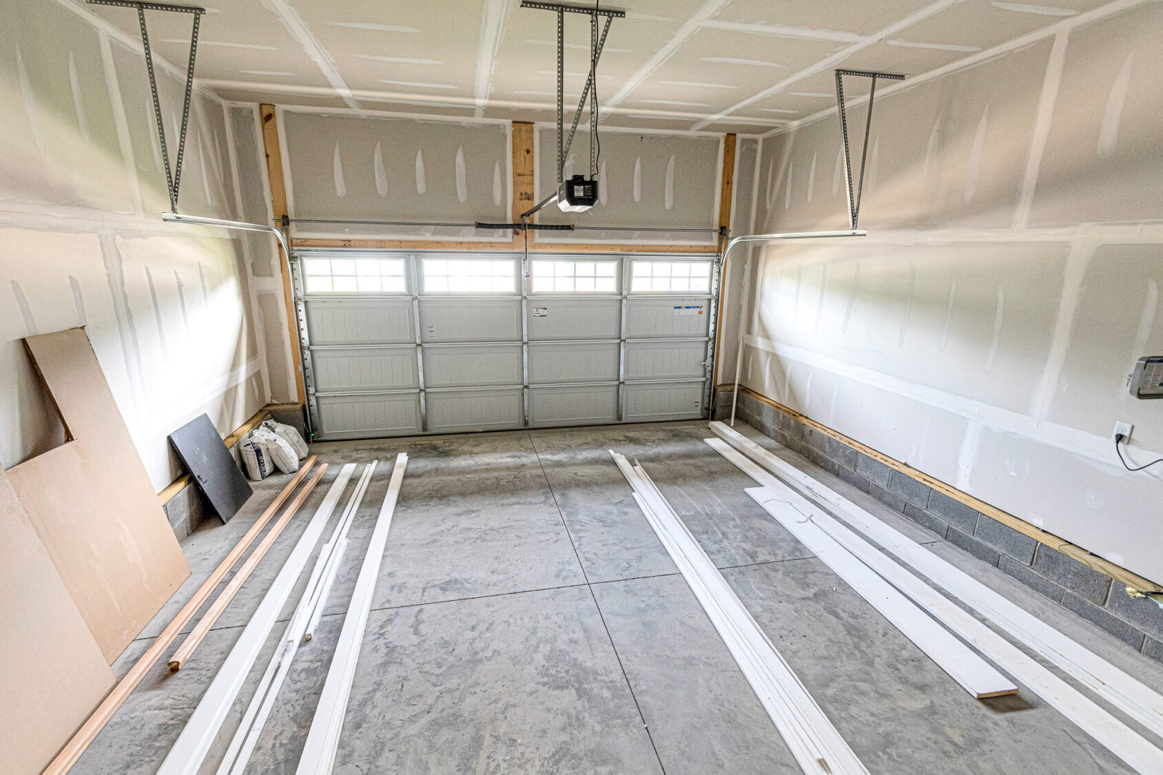 Empty garage at Somerset Hill Lot 8, unfinished walls and ceiling, white boards and wood planks on concrete floor.