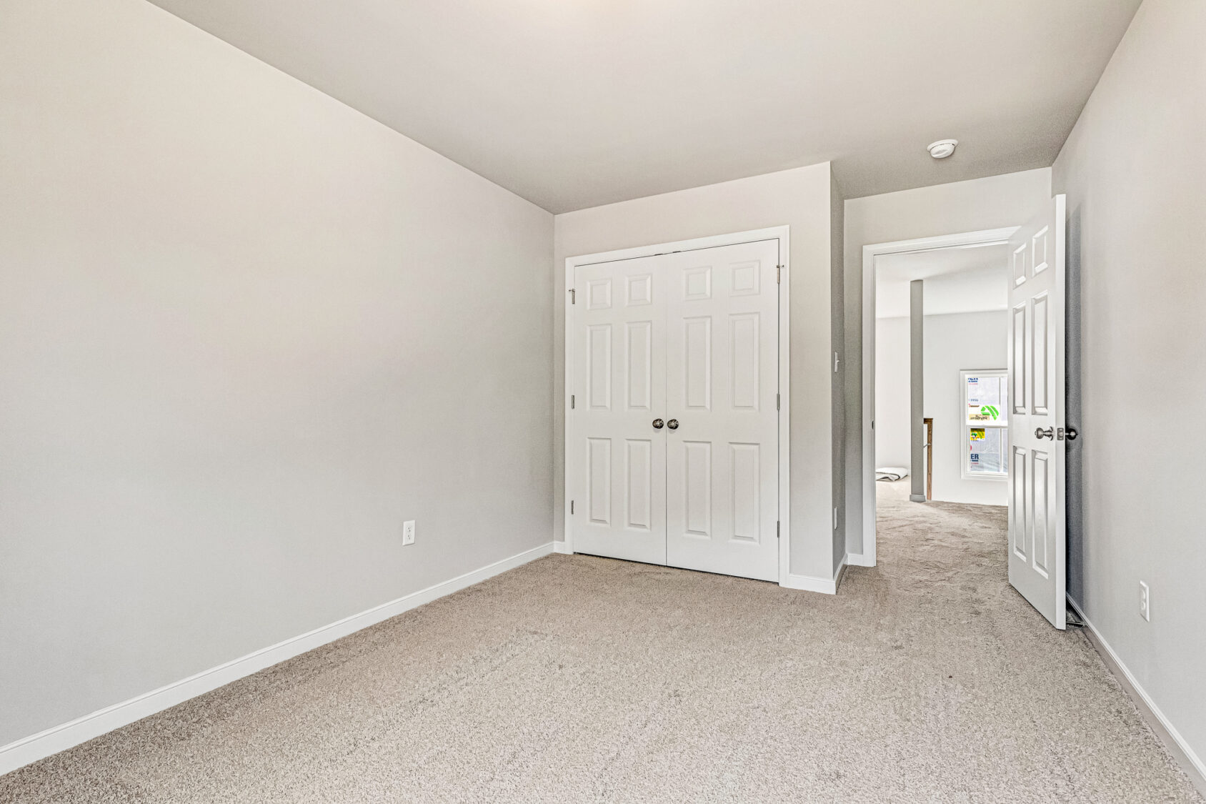 Bright, empty room in Somerset Hill with beige carpet, white walls, double closet doors, and an open hallway door.