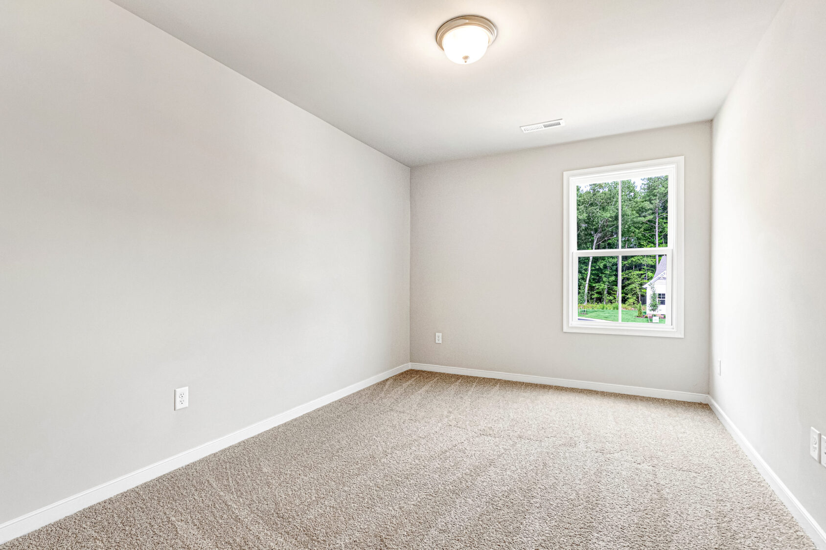 Empty, carpeted room on Somerset Hill Lot 8 with light gray walls, ceiling light, and a window showing greenery.