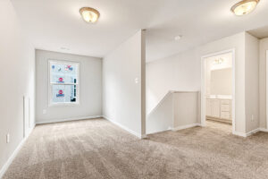Carpeted Somerset Hill room with window, ceiling lights, and open doorway to bathroom with sink and mirror. Lot 8.