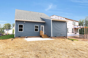 Blue house with back porch and steps on Somerset Hill, Lot 8, beside a partially built home; straw covers the yard.