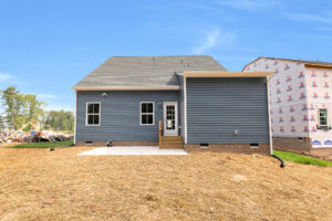Blue house with white trim on Lot 8, small porch, bare yard, beside a partially built home in Somerset Hill.